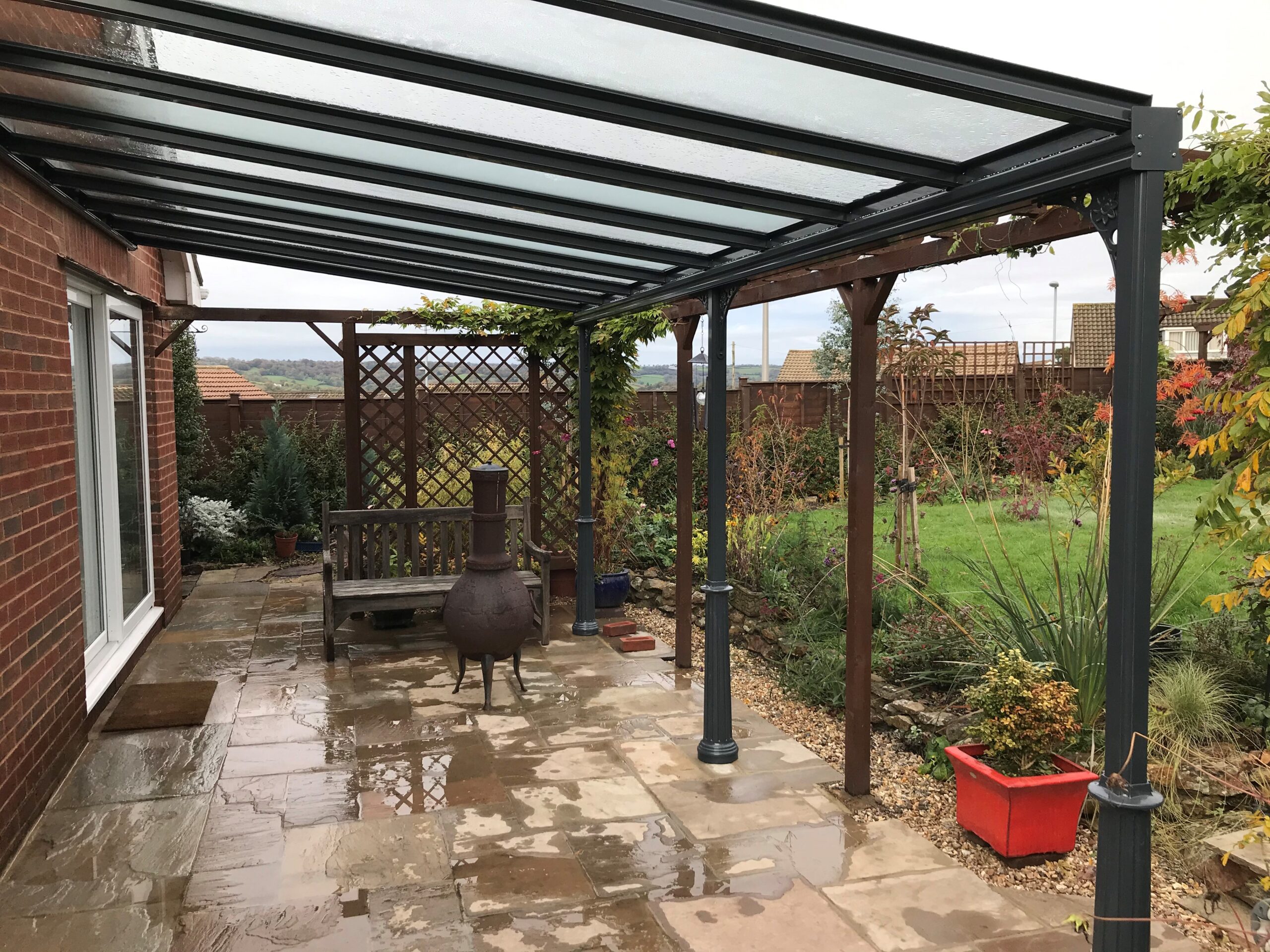 Traditional Glass Veranda roof on a bungalow in Honiton, Devon and powder coated in anthracite grey with ornate Victorian posts, gutter and gallows brackets by All Weather Canopies South West Ltd