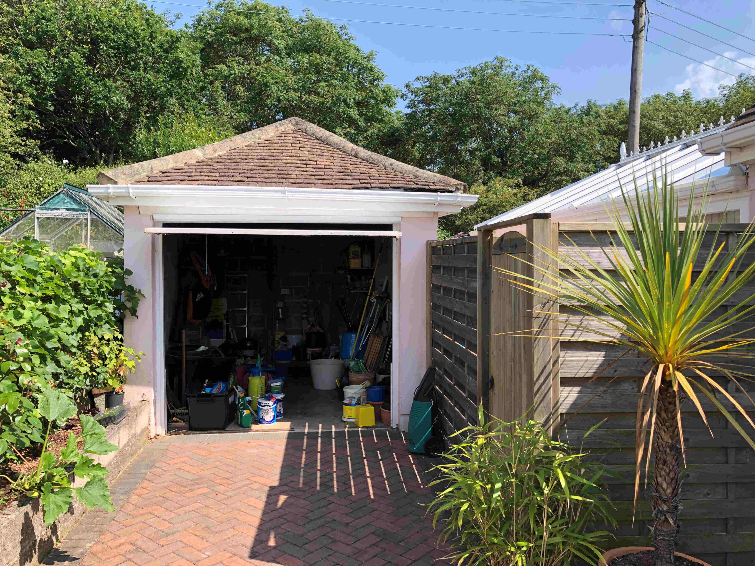 Pink garage in Paignton, Devon with white guttering and a brown tiled roof, set beside greenery and a wooden fence; a residential outbuilding scene