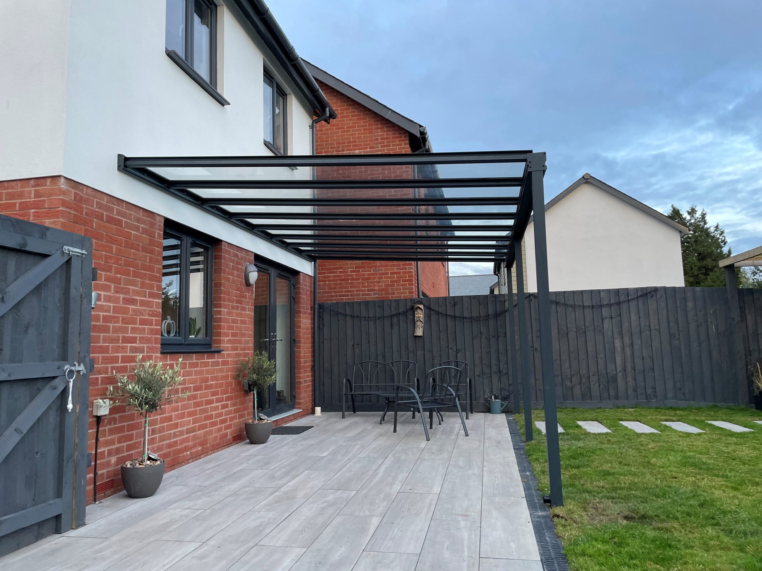 Simplicity 6 veranda in anthracite grey featuring toughened clear glass roofing installed on a red brick house in South Molton, Devon, by All Weather Canopies