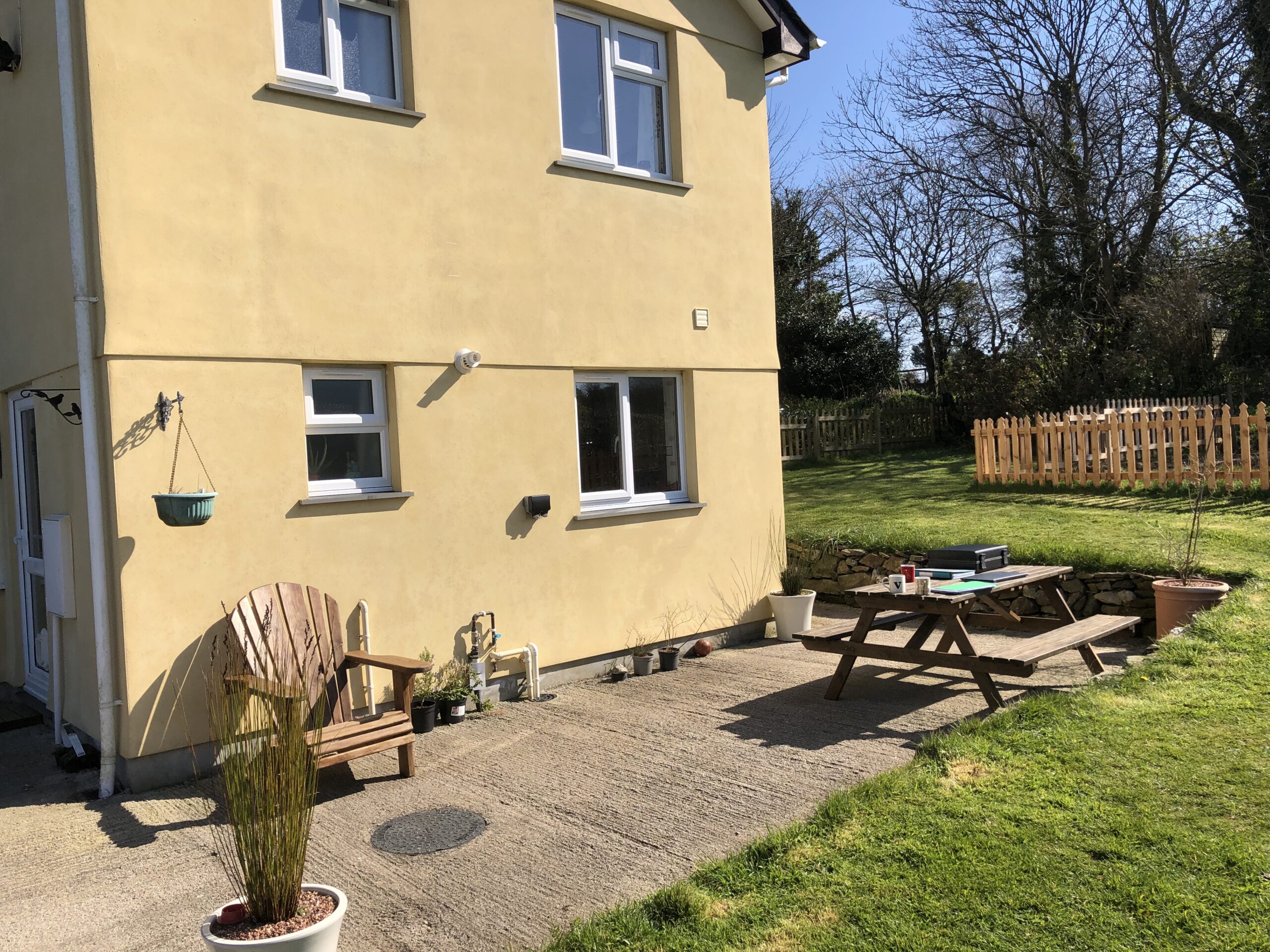 Exterior view of a yellow house in Hayle, Cornwall with a patio area and garden furniture.