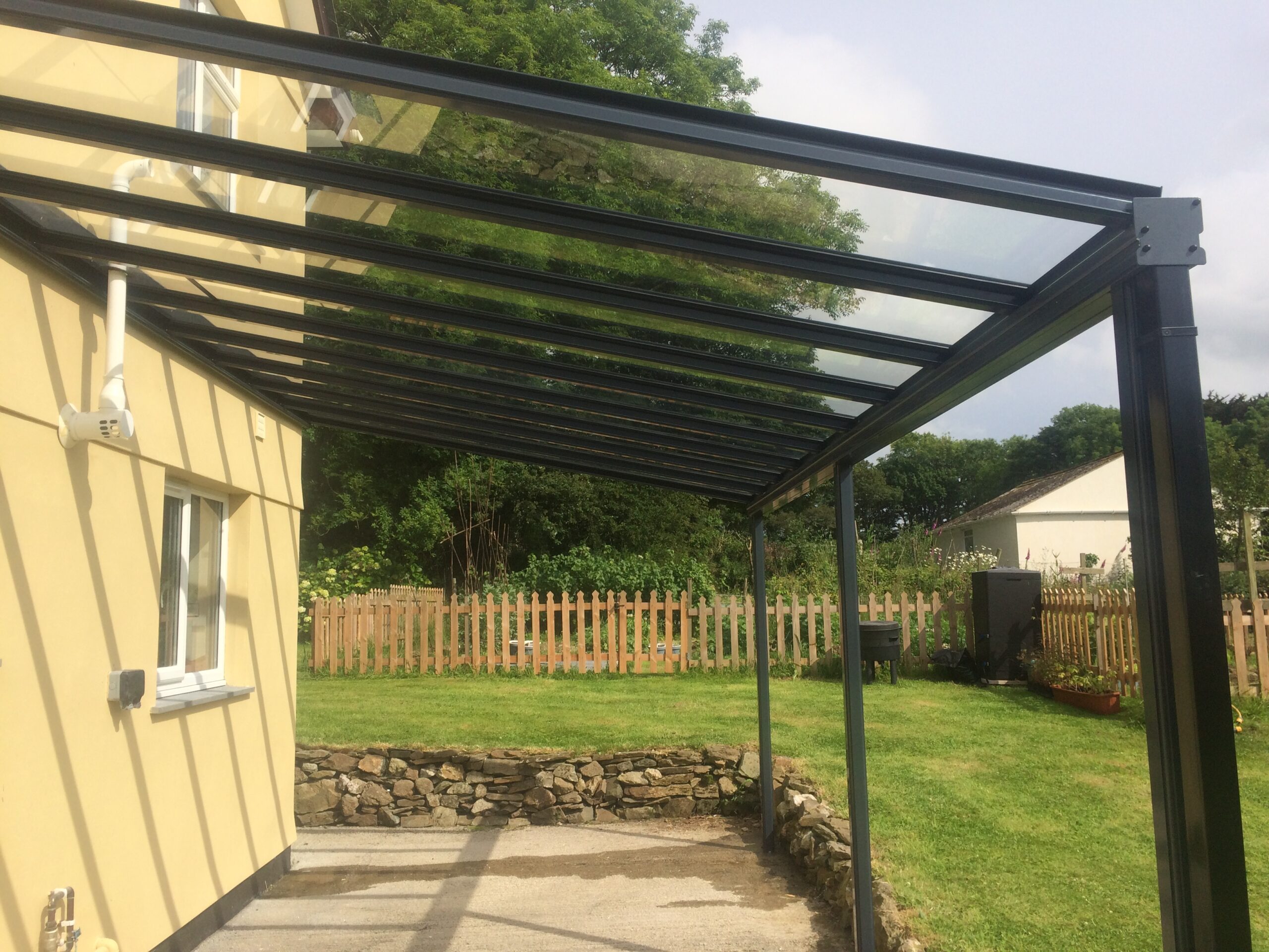 Glass veranda canopy structure with a black frame attached to a yellow building.