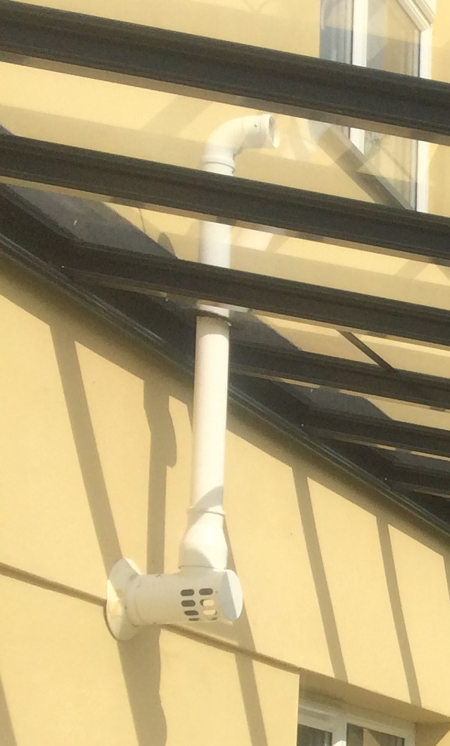 White gas flue pipe attached to a canopy structure against a yellow wall.