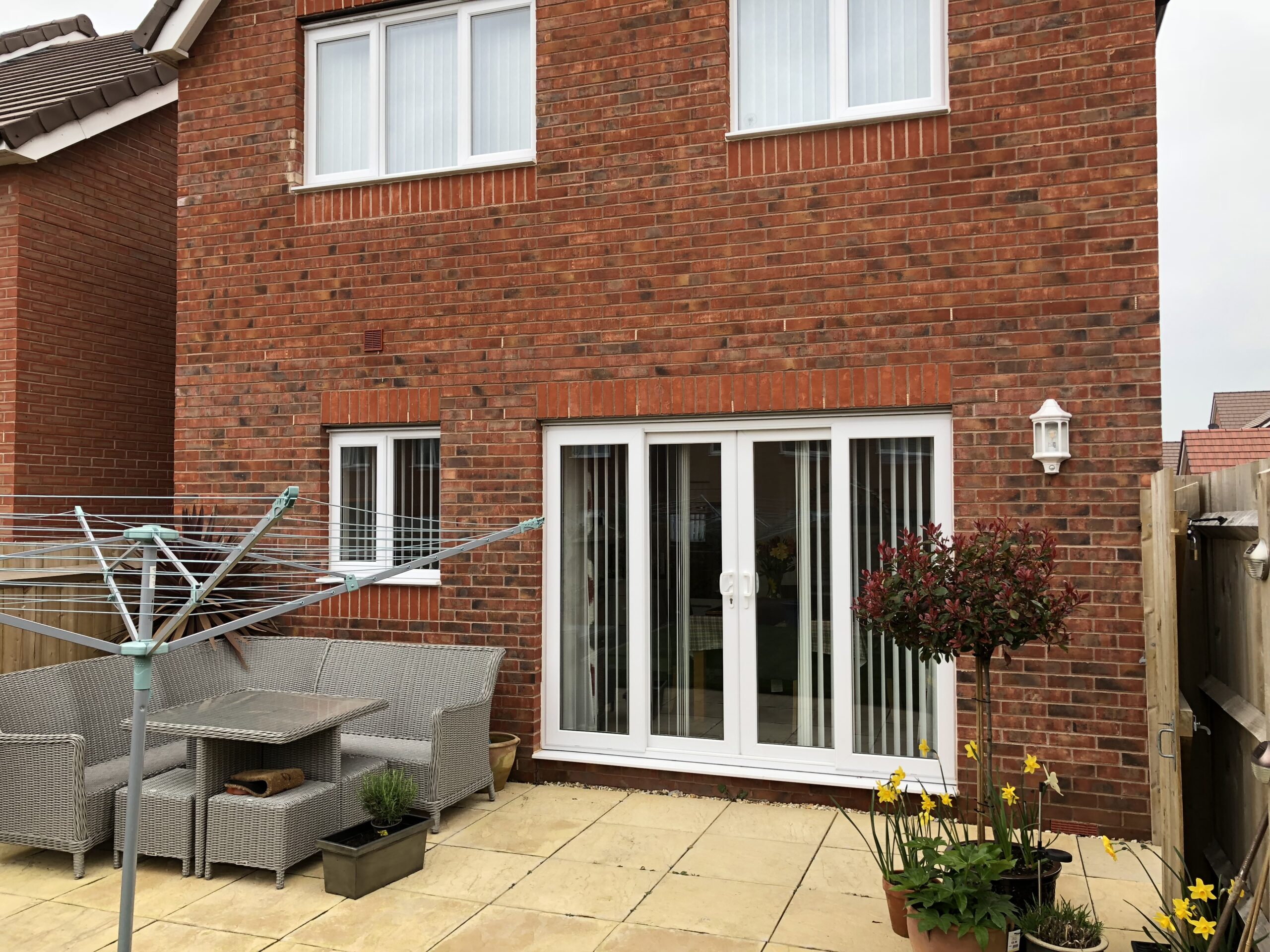 A red brick house featuring large sliding doors and a patio area with garden furniture and plants.