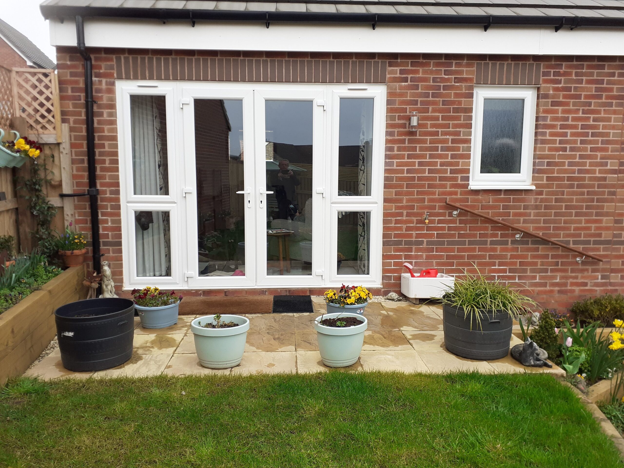 Double doors leading to a house, flanked by various planters and a small garden area.