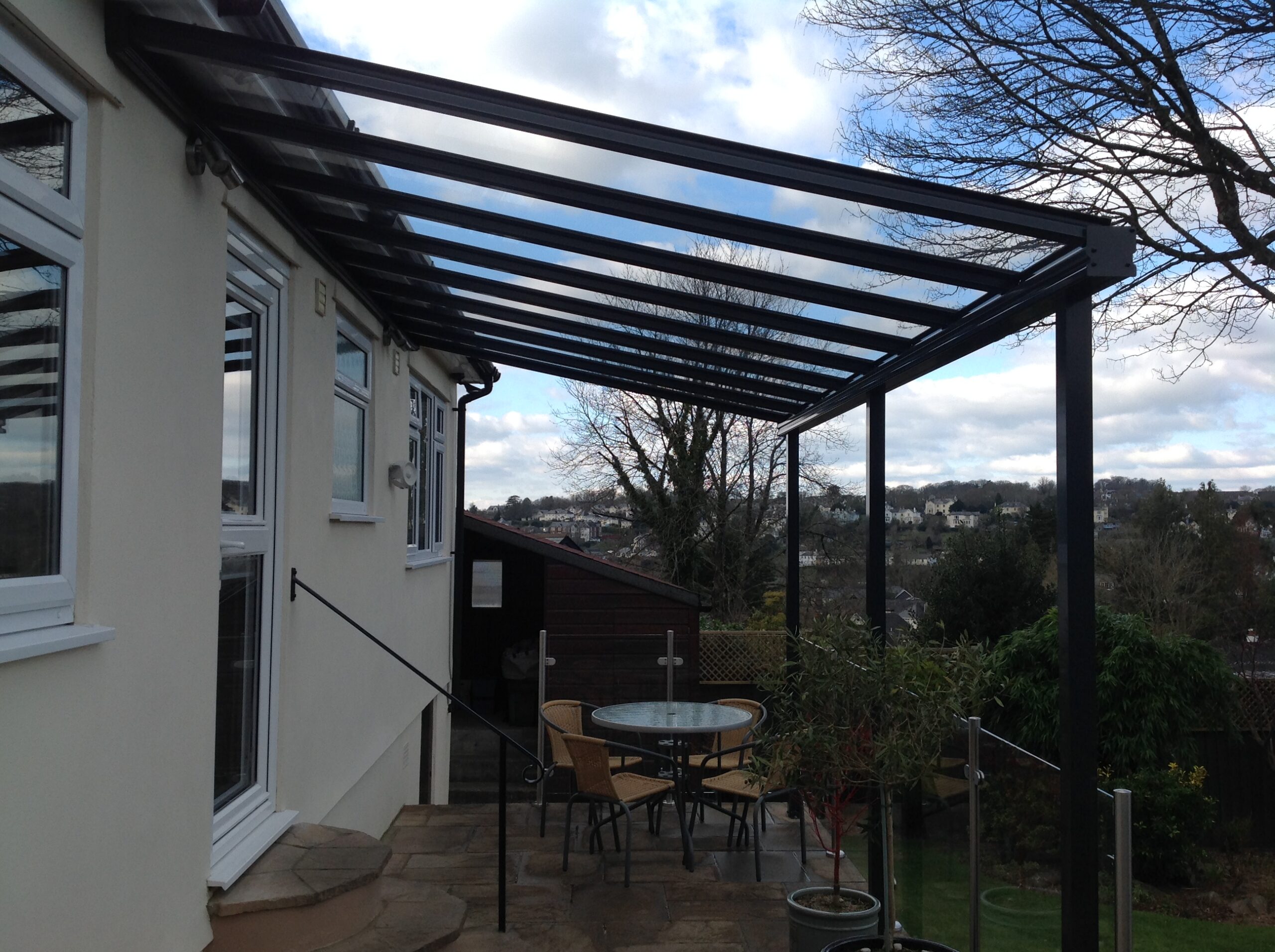 Glass patio veranda canopy with a black frame attached to a residential building.