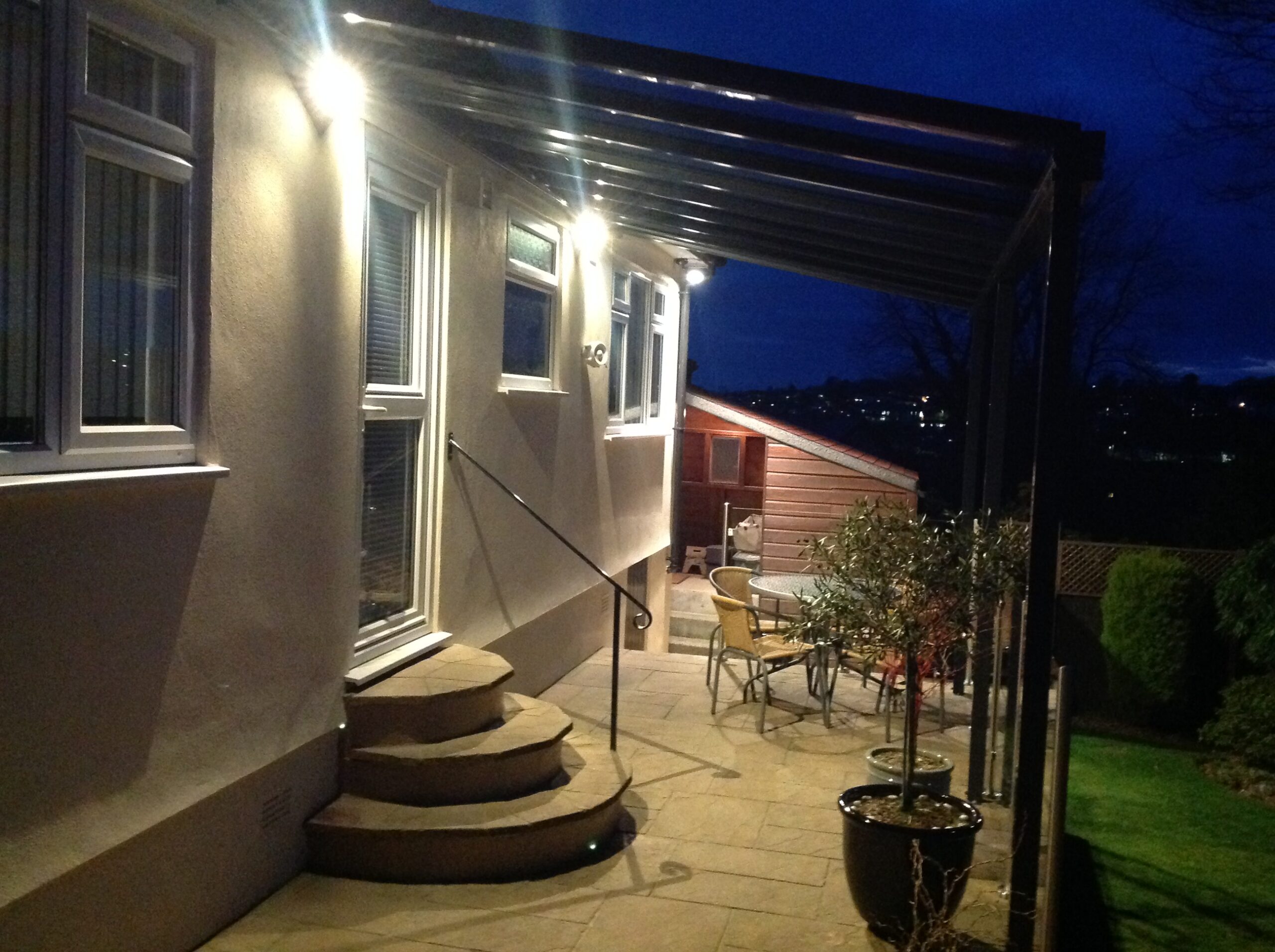 Glass patio veranda canopy attached to a house with outdoor seating and lighting.