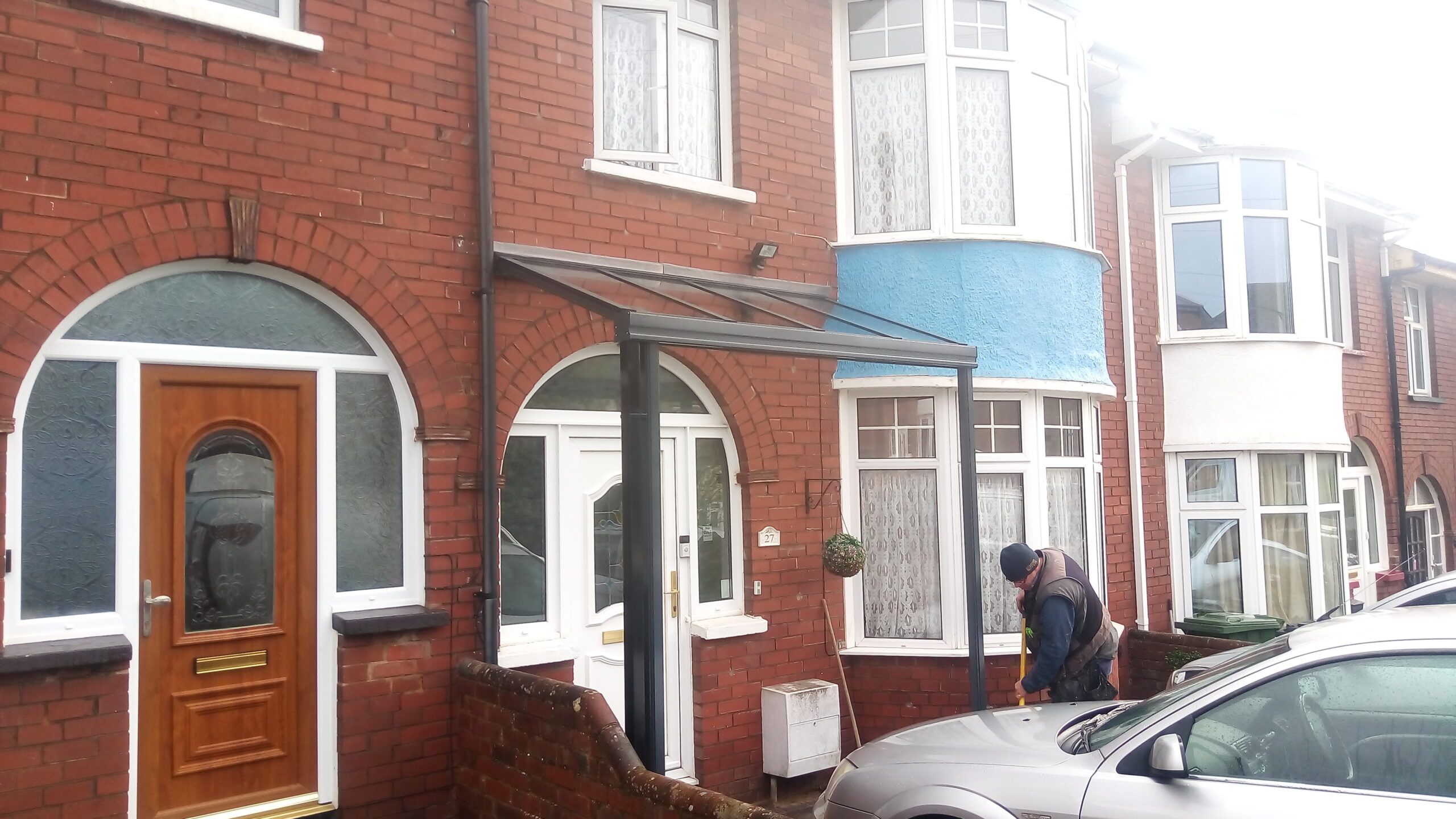 Glass veranda canopy installed at the entrance of a residential property with brick facade.