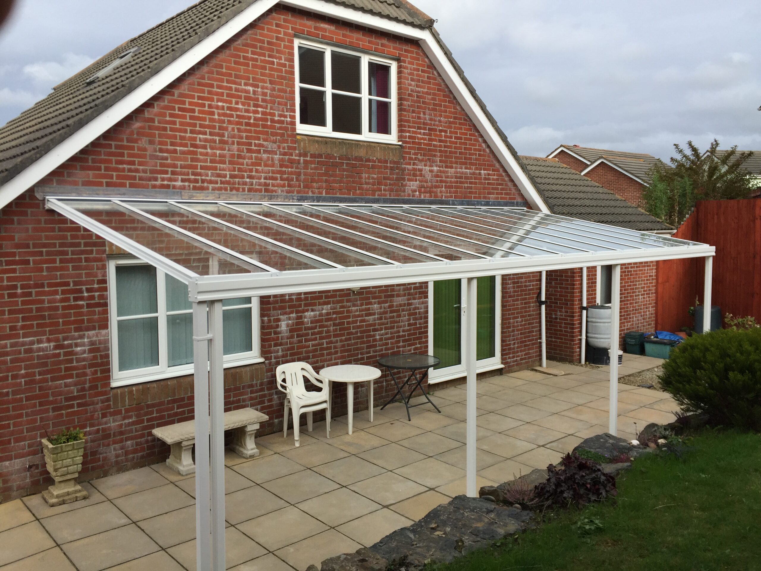 Glass veranda canopy structure attached to a brick house with a patio area.