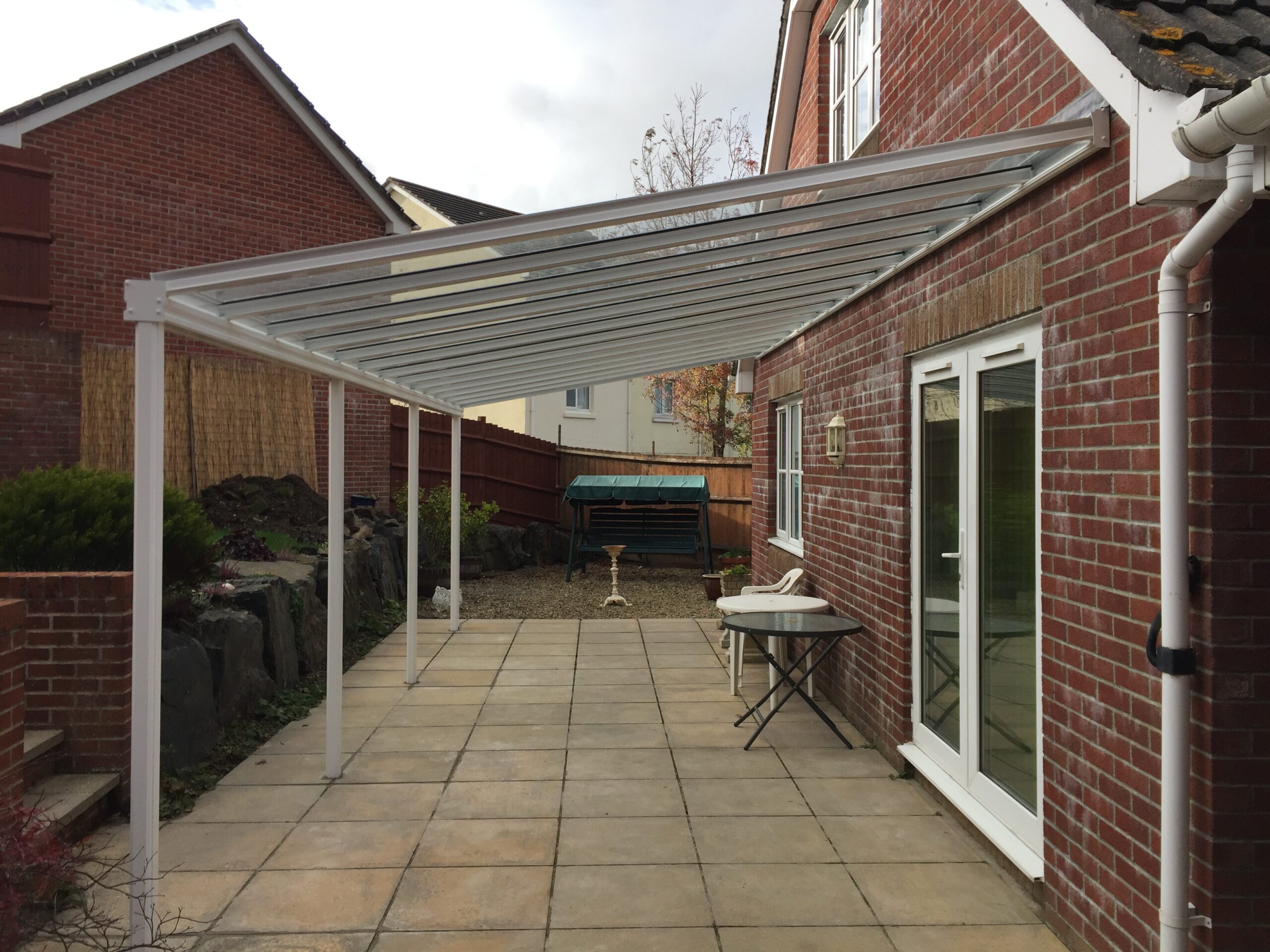 A glass veranda canopy structure with a metal frame installed in a residential outdoor area.