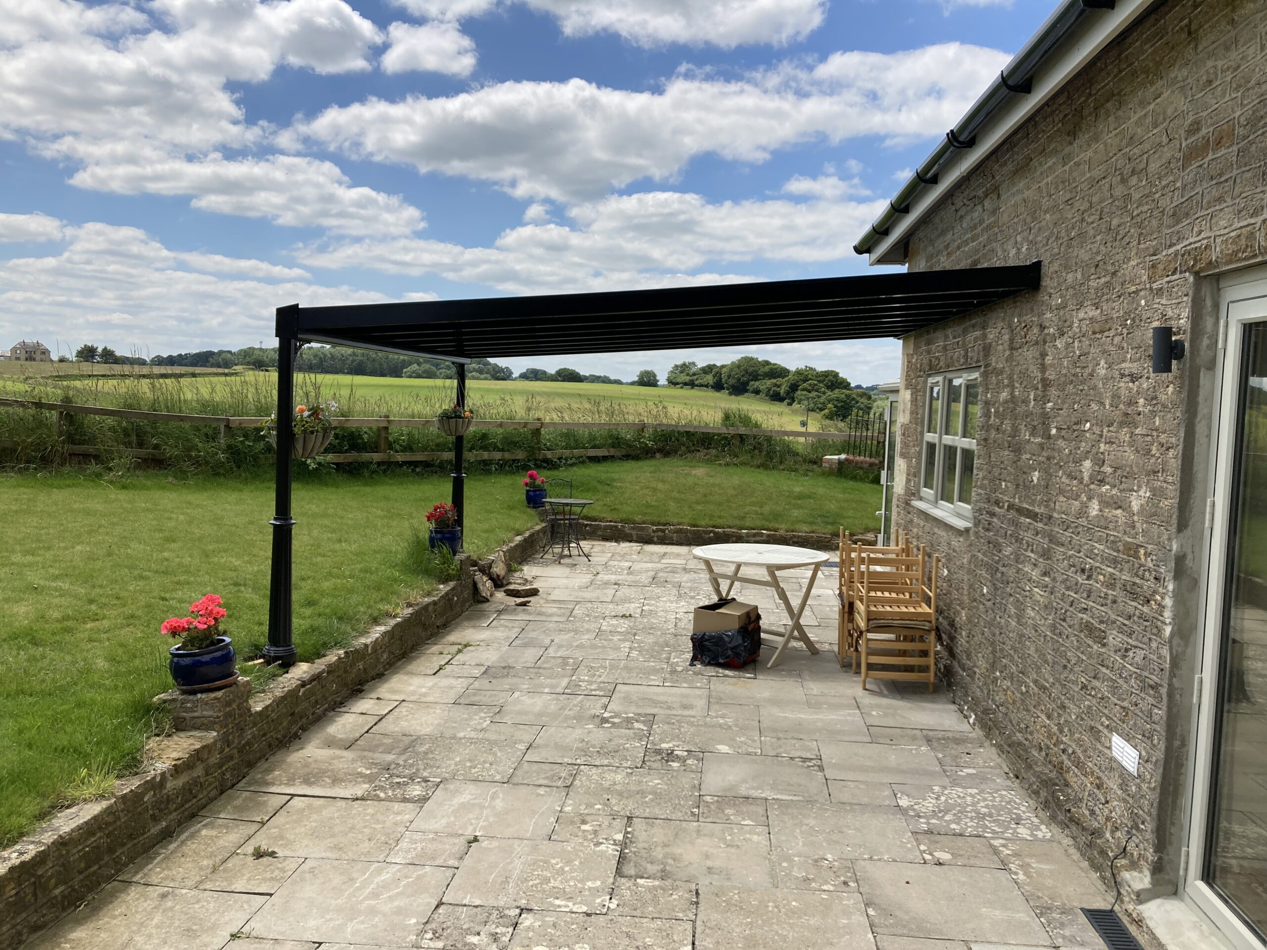 Jet black glass roof canopy structure attached to a stone building with outdoor seating area.