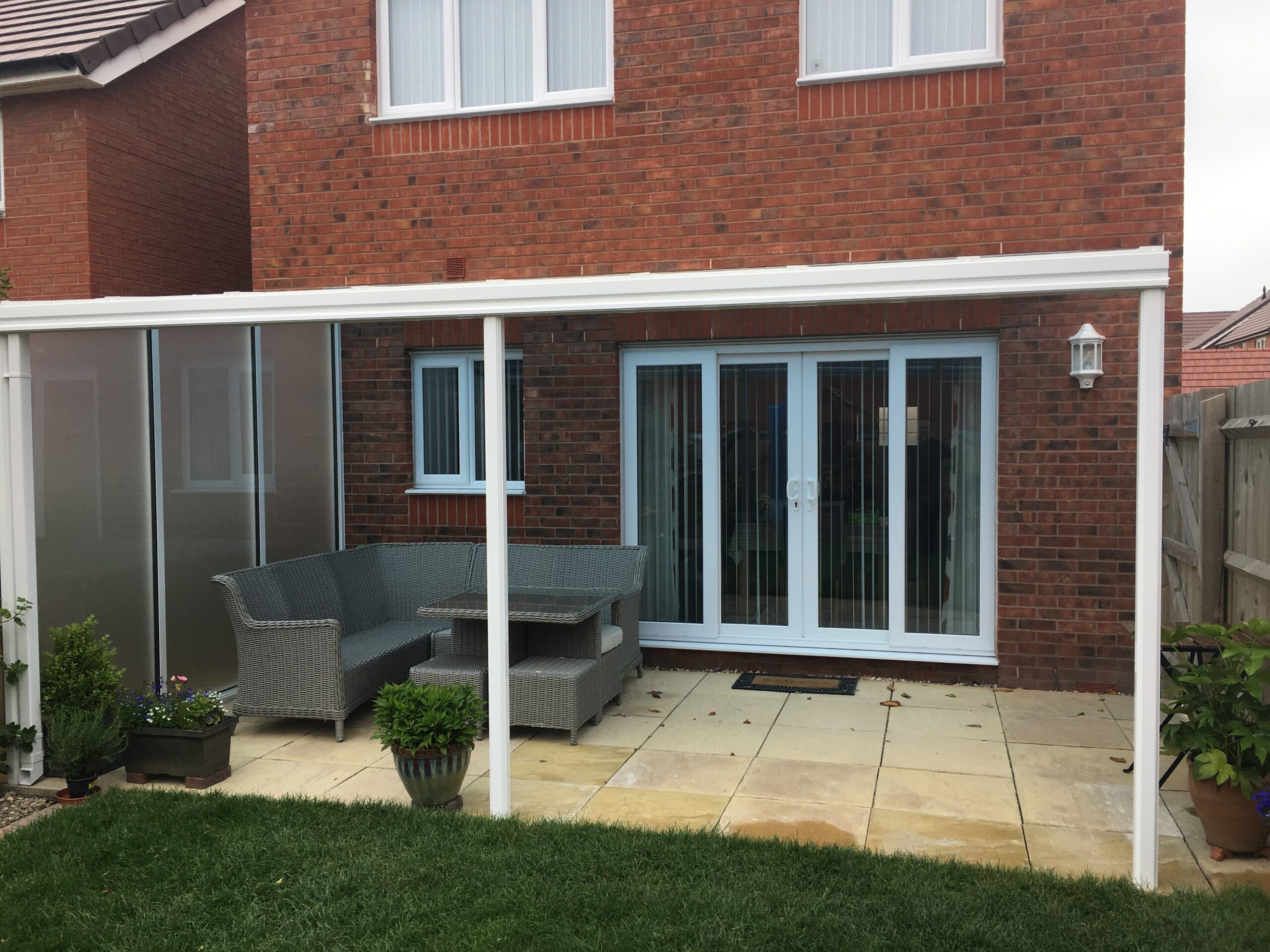 Veranda canopy structure with glass panels and outdoor seating area in a residential setting.