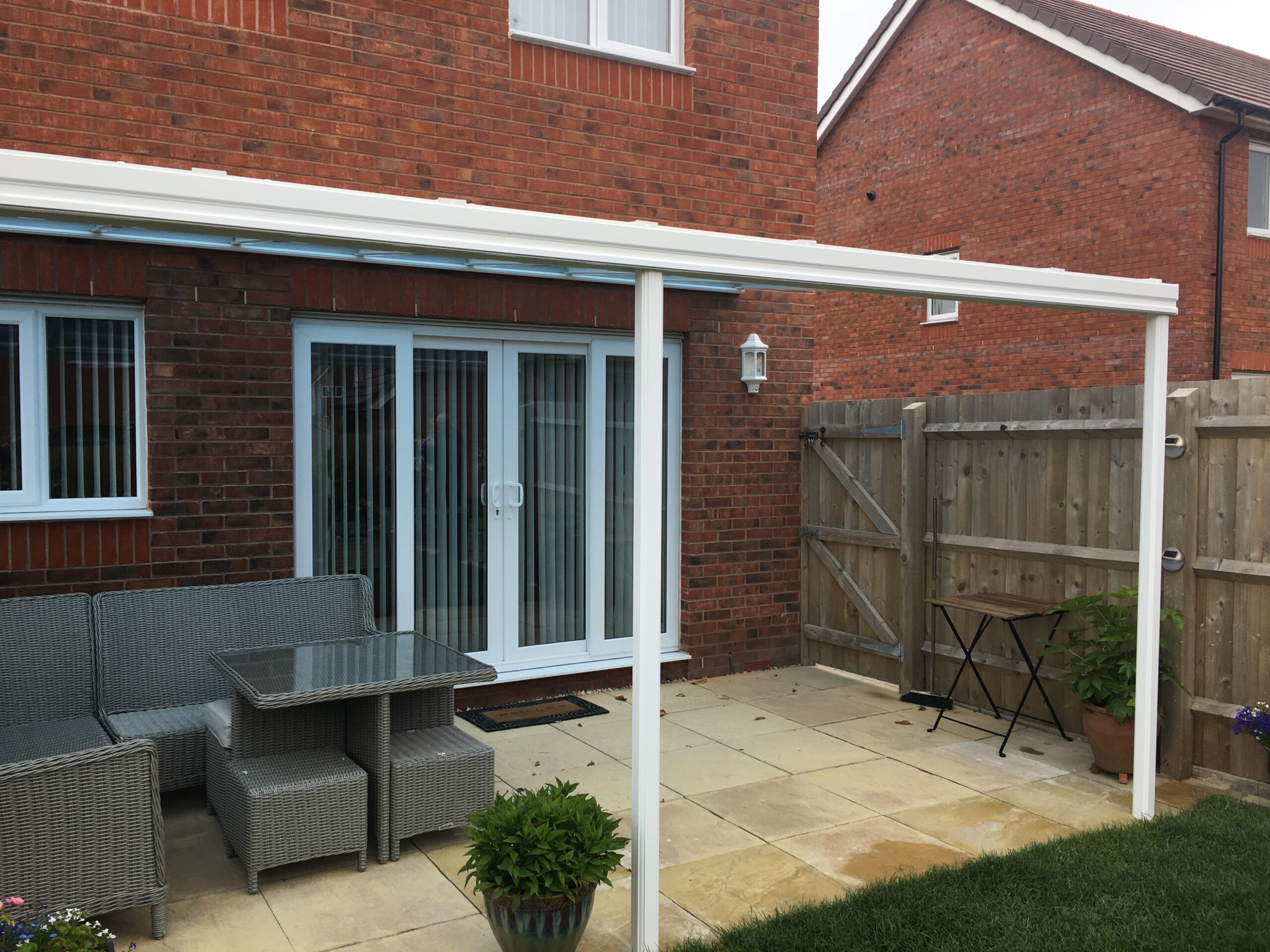 Veranda canopy with a glass roof structure attached to a brick house in a residential area.