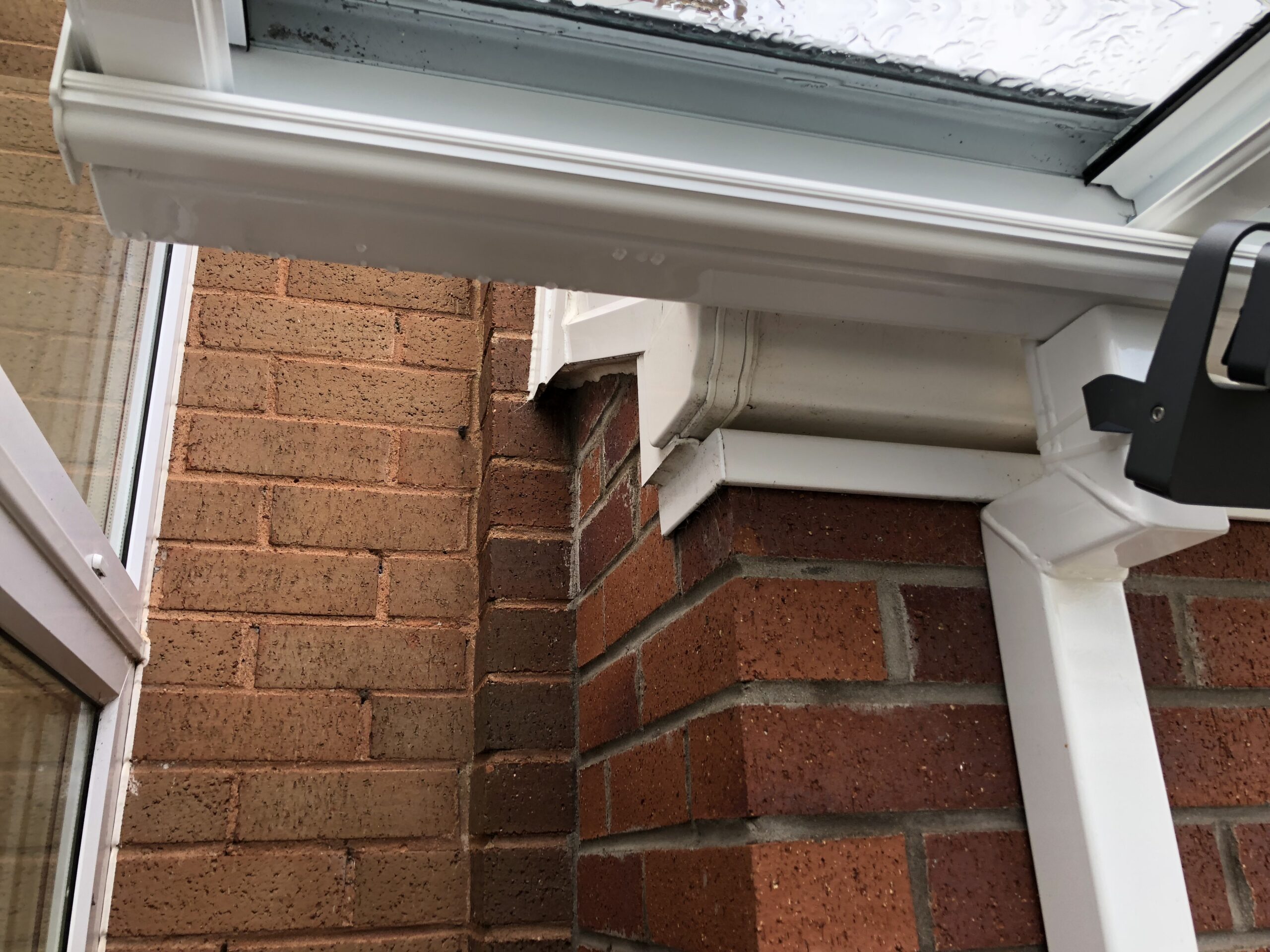 Veranda canopy with a glass roof installed on a brick wall, showing structural details and water droplets.