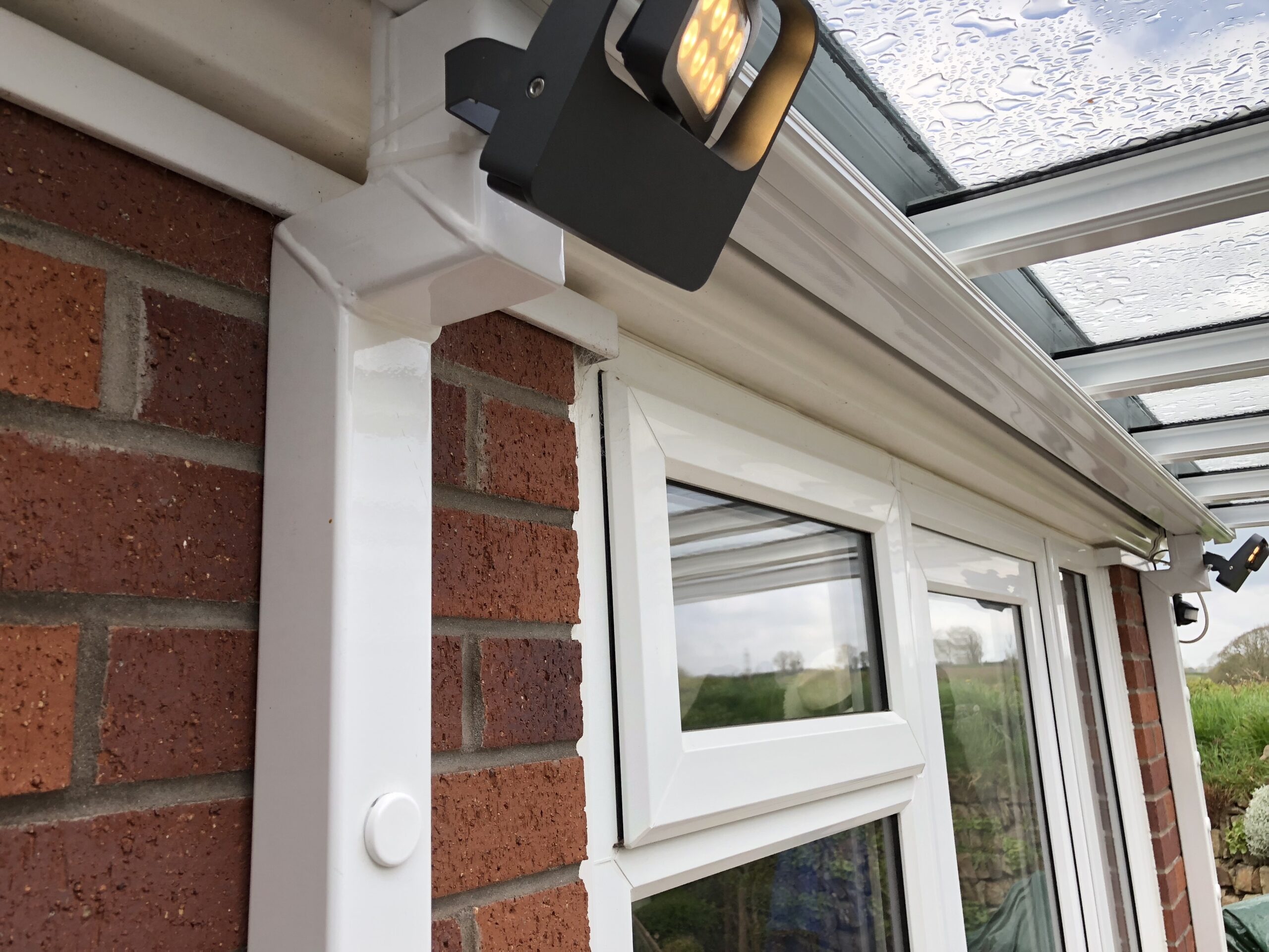 Veranda canopy with a glass roof and integrated lighting mounted on a brick wall.