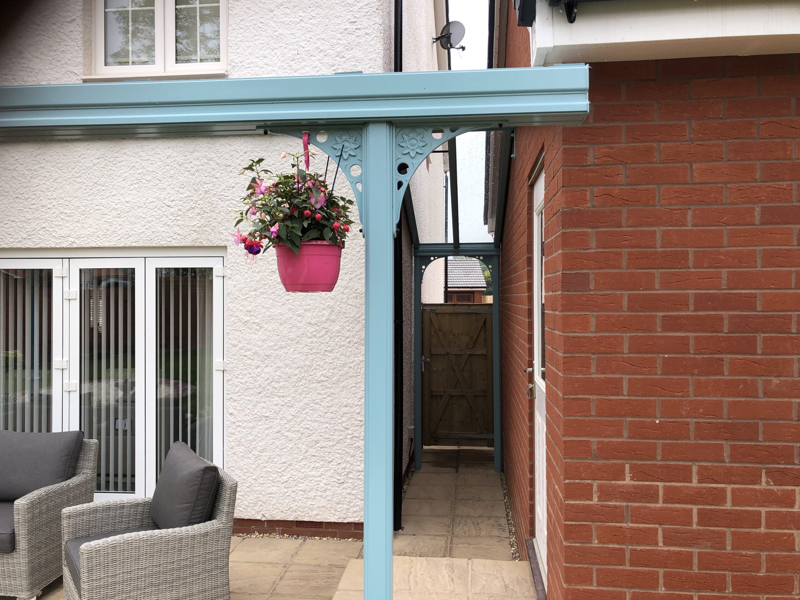 Pastel turquoise veranda canopy with a glass roof attached to a brick wall, featuring decorative supports.